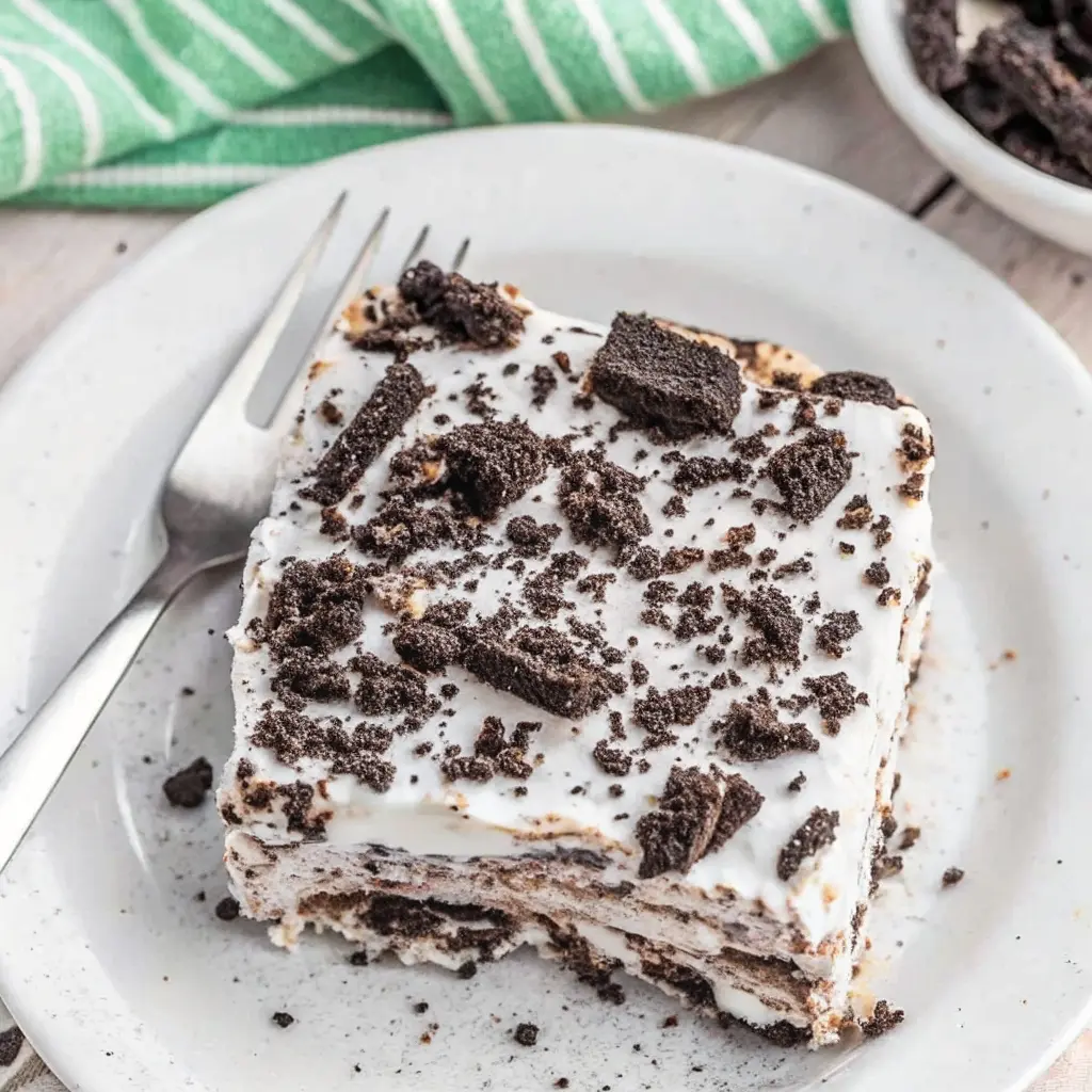 Cookies and Cream Ice Cream Cake – Easy No-Bake Frozen Favorite 2 Oreo cookie layered icebox cake slice with whipped topping on white plate