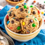 Scoops of monster cookie dough with colorful candy-coated chocolates in a white-striped bowl